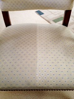 Close-up of a patterned chair cushion, showcasing clean and stained sections of fabric, with wooden chair frame.
